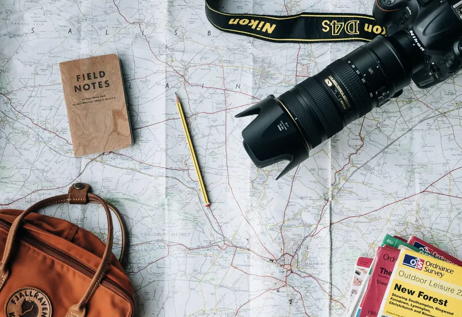 Mapa de viaje con cuaderno, cámara y mochila sobre una mesa